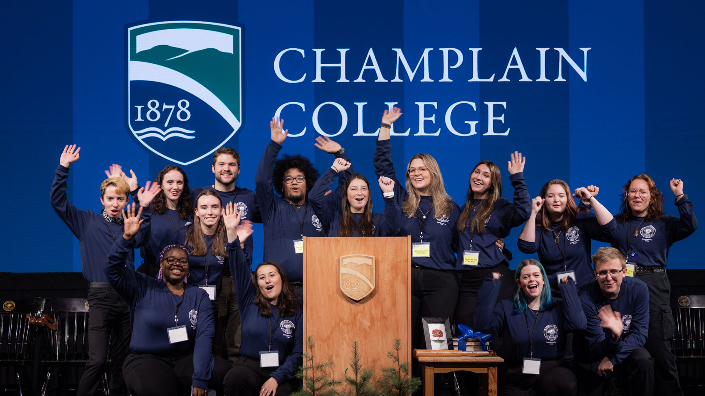 A group of students pose enthusiastically with school spirit, in front of a Champlain College banner