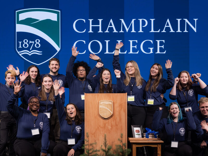 A group of students pose enthusiastically with school spirit, in front of a Champlain College banner