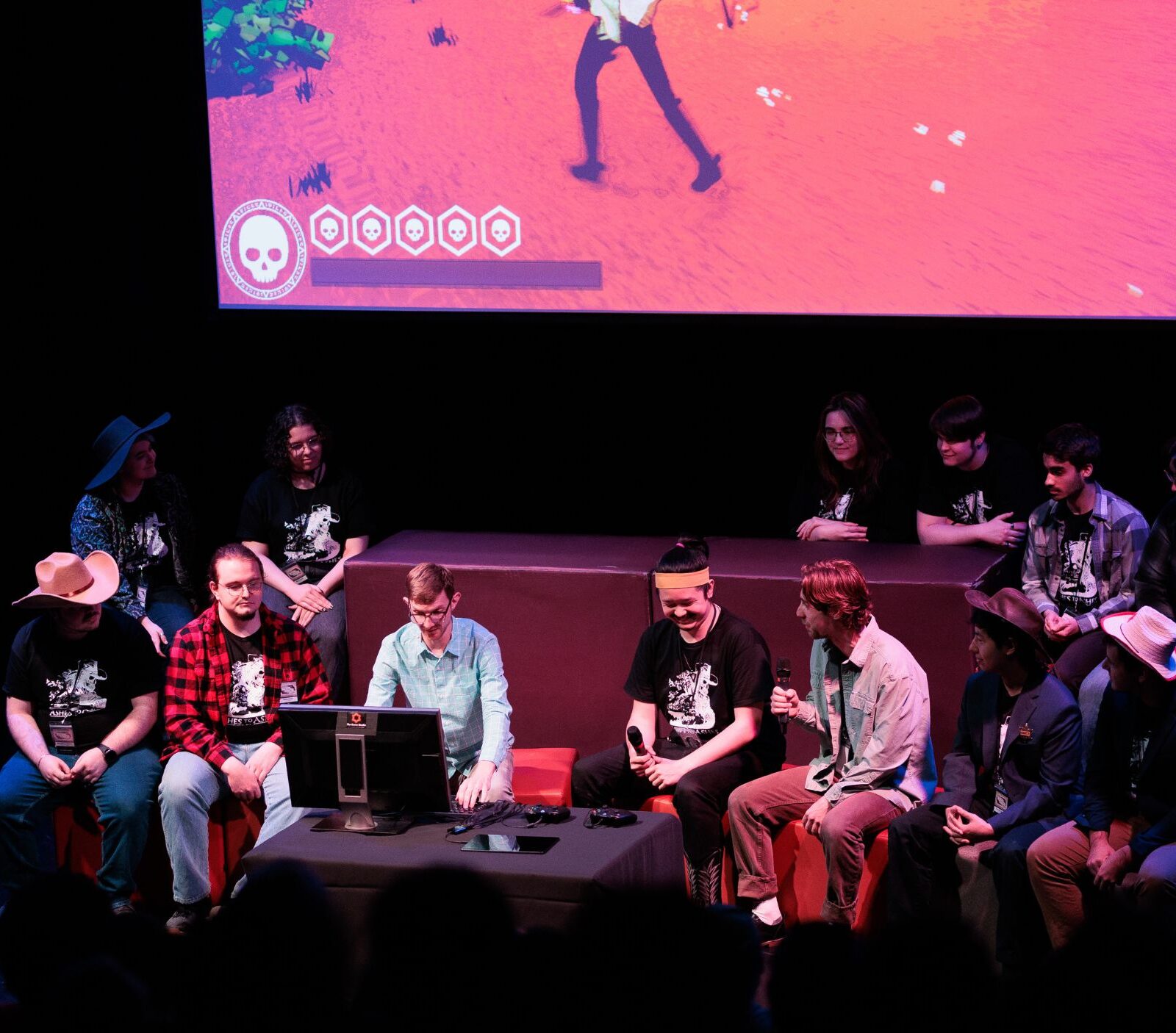 A group of students sit together in front of a screen, presenting their game.