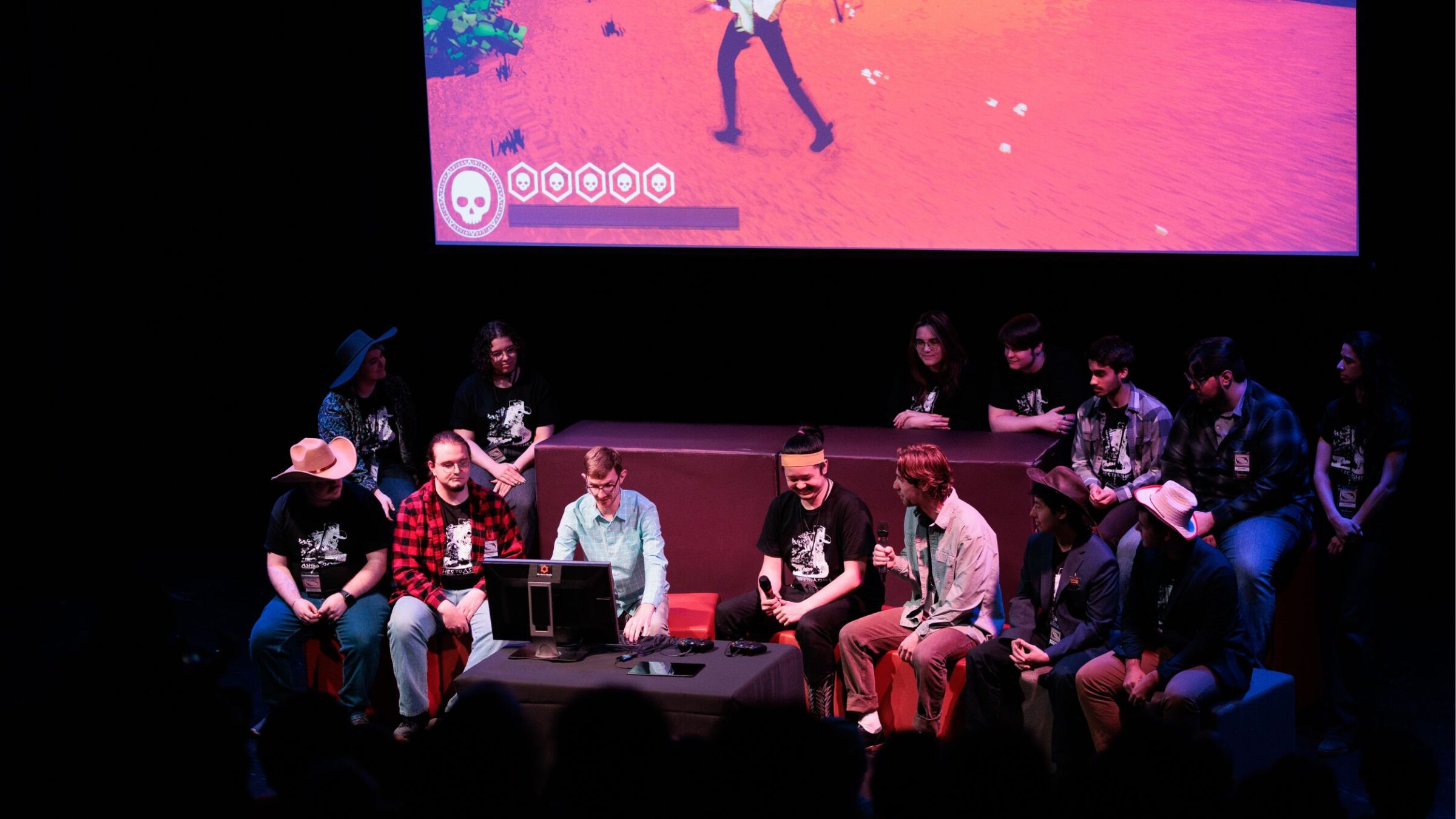 A group of students sit together in front of a screen, presenting their game.