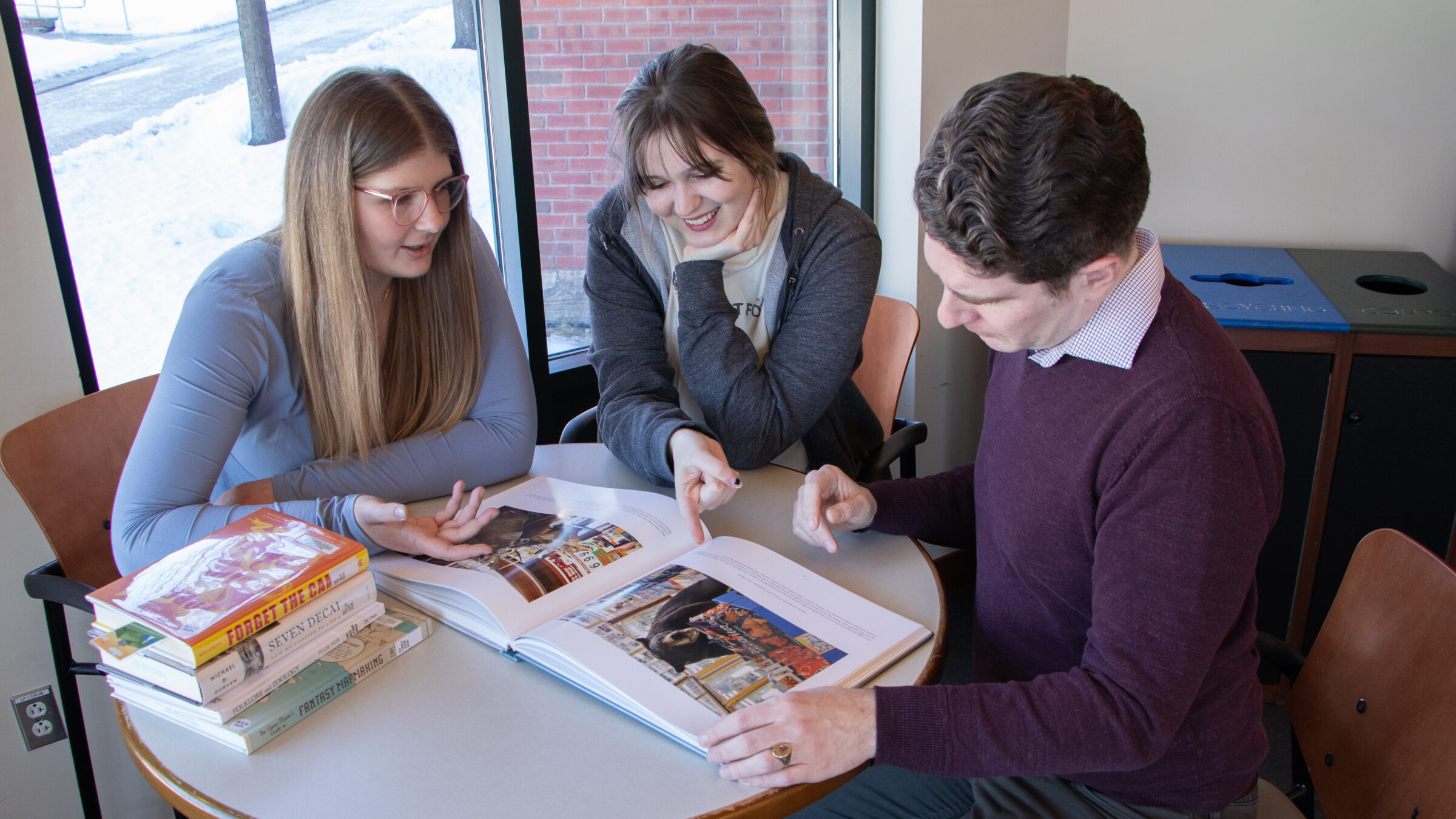 Two students and a librarian look through a book together during a research help appointment.