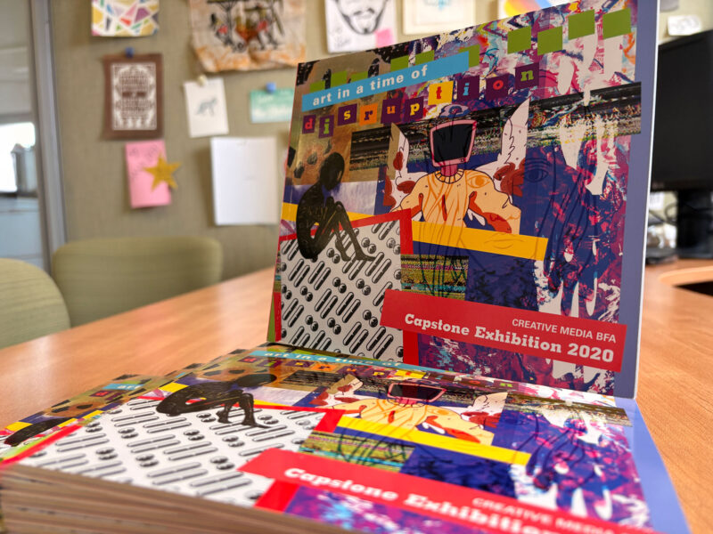 A stack of colorful books showcasing Creative Media student artwork