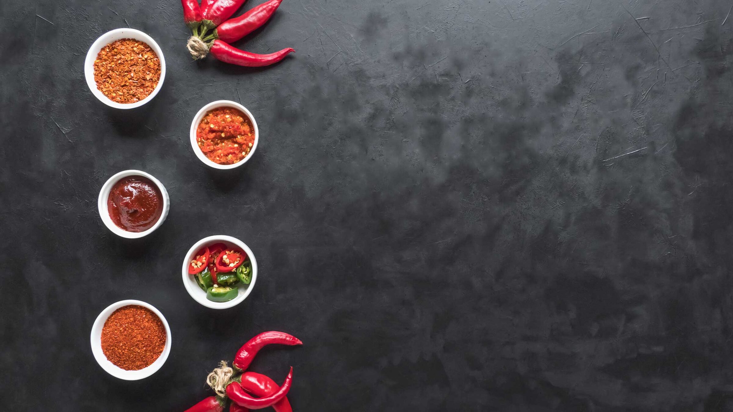 hot sauce samples and hot peppers on a dark background