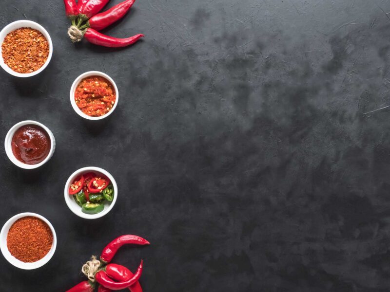 hot sauce samples and hot peppers on a dark background