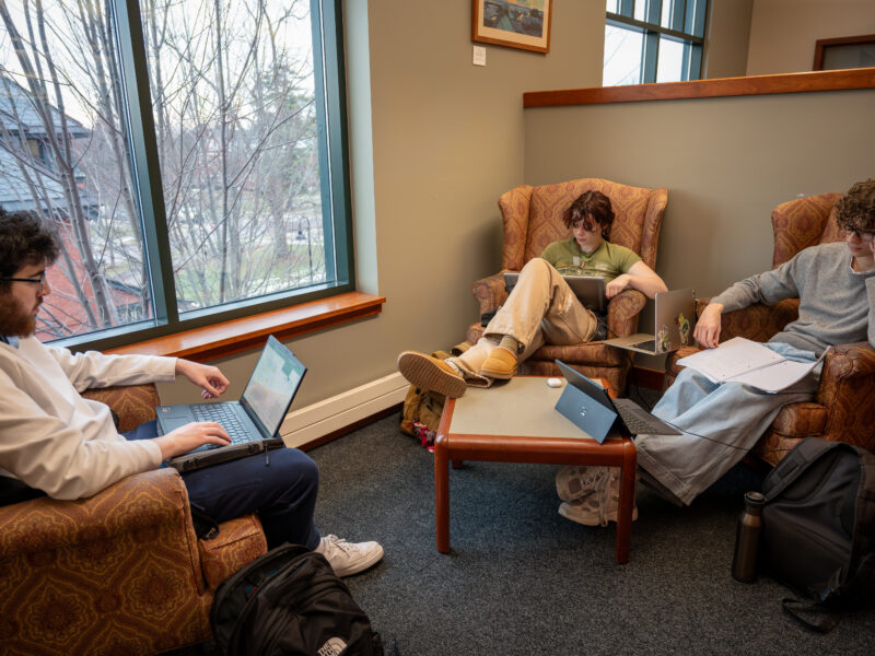 Three students study on laptops in armchairs in the Miller Information Commons.