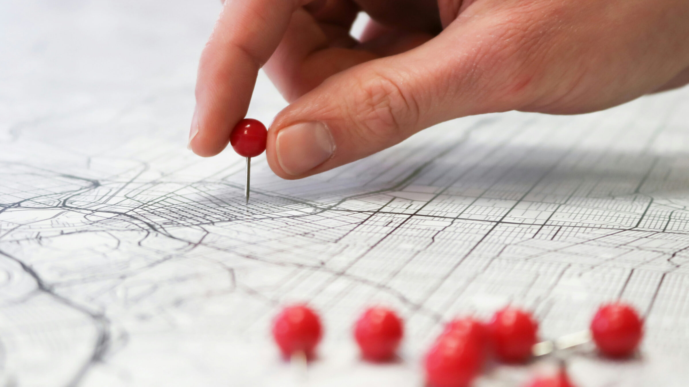 A hand placing a red pin into a black and white paper map