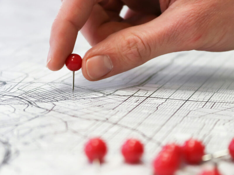 A hand placing a red pin into a black and white paper map