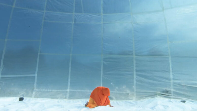A person wearing an orange outfit in a bubble outside during the day