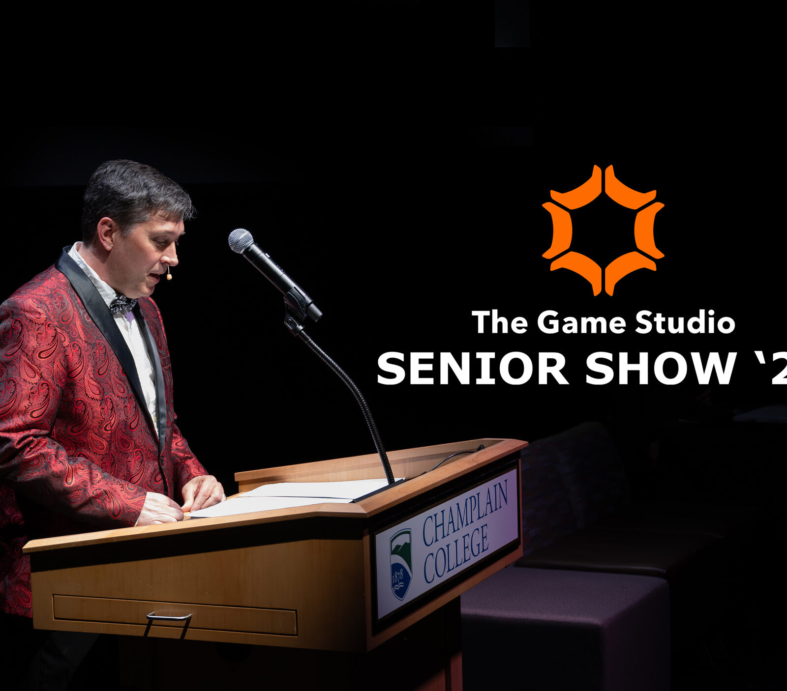 Presenter standing at the podium announcing the 2026 Game Senior Show against a black background and the game studio logo