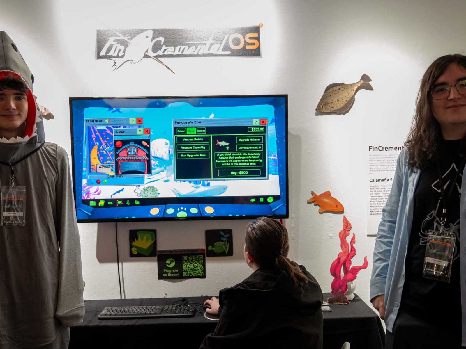Students dressed up in themed clothing standing in front of the gallery showcase of FincrememntalOS, a 2026 senior showcase game