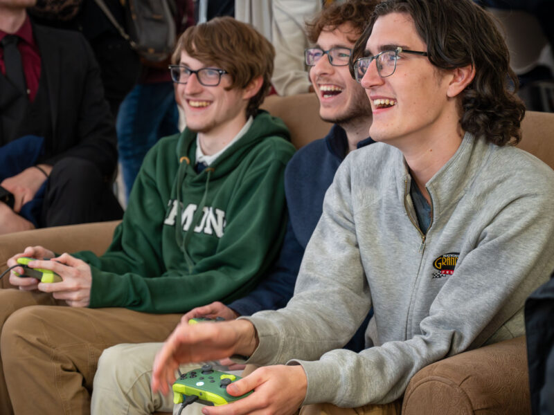 Students smiling and playing a game on controllers while sitting out a couch during Game Senior Show 2026