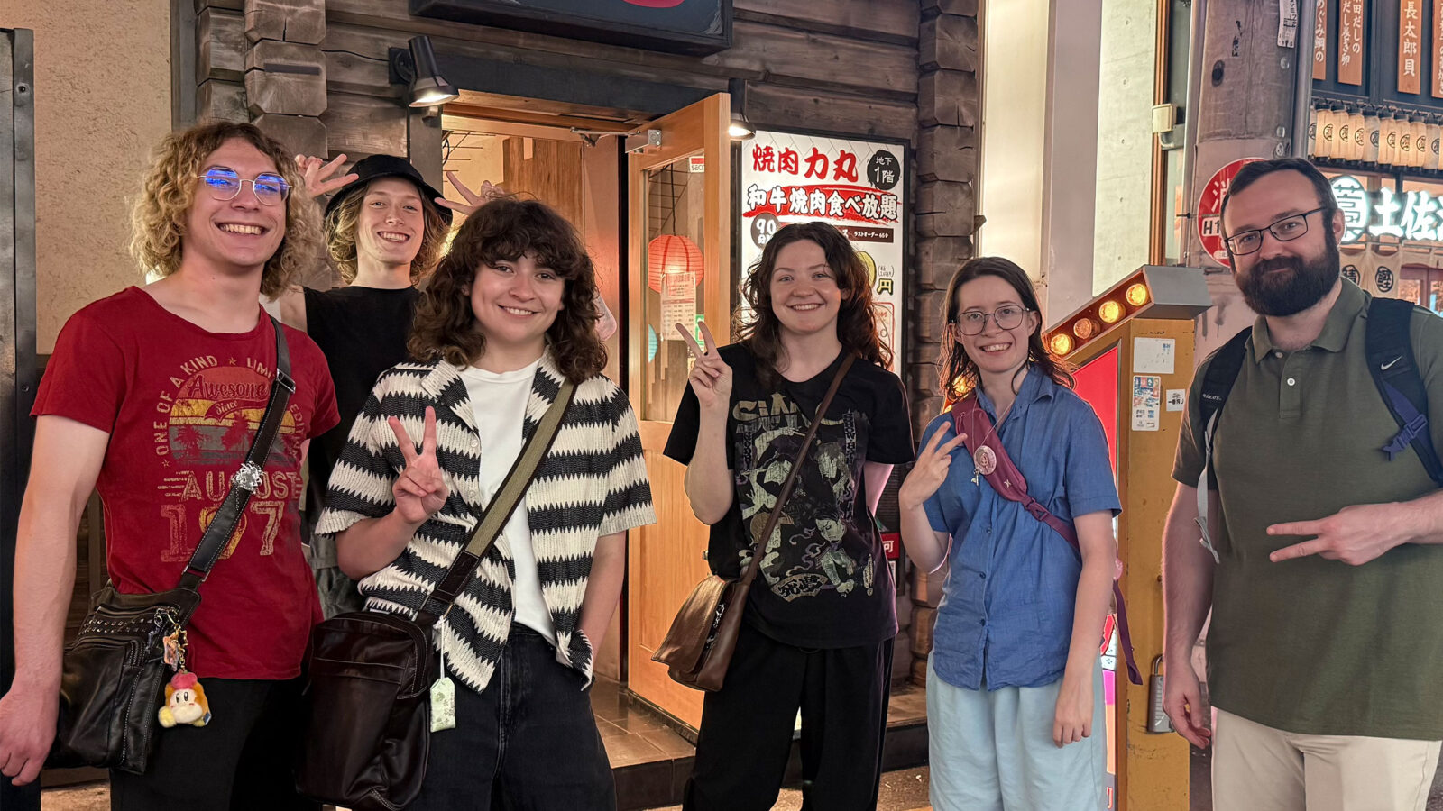 six students smile at the camera hand signaling peace signs