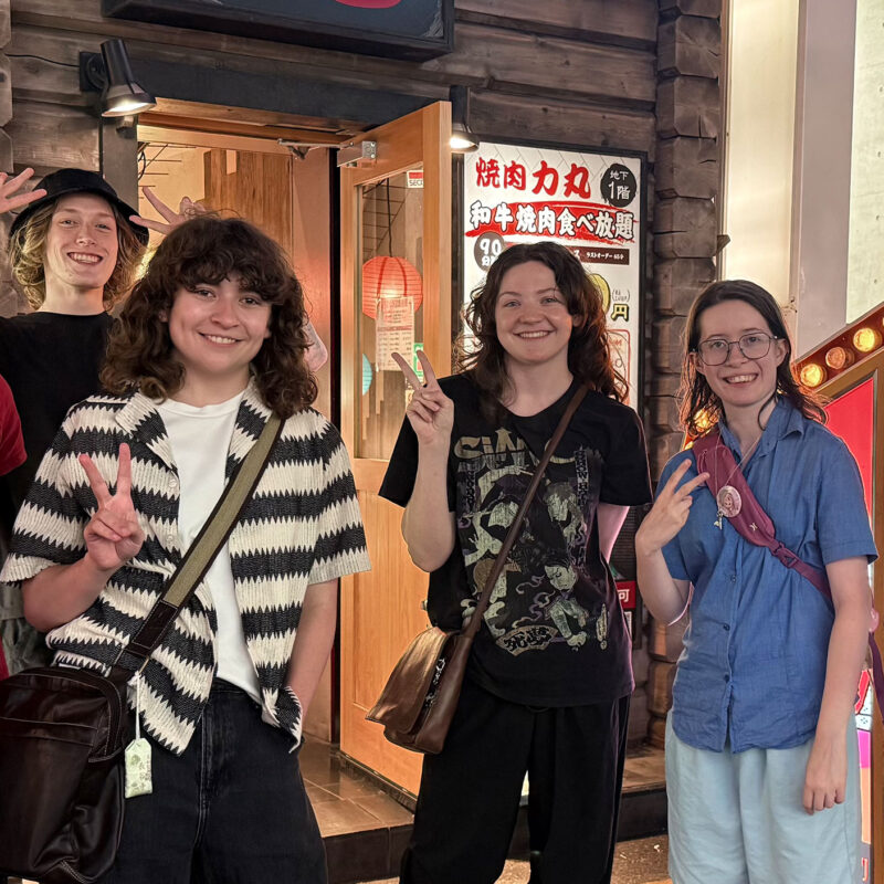 six students smile at the camera hand signaling peace signs