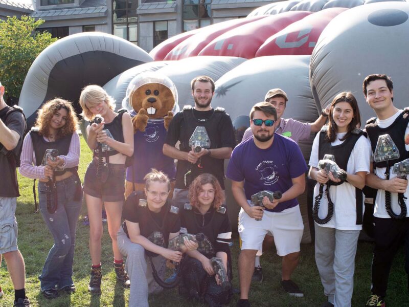 Chauncey and students posing for a photo in front of a blow up bounce house wearing greys and purples