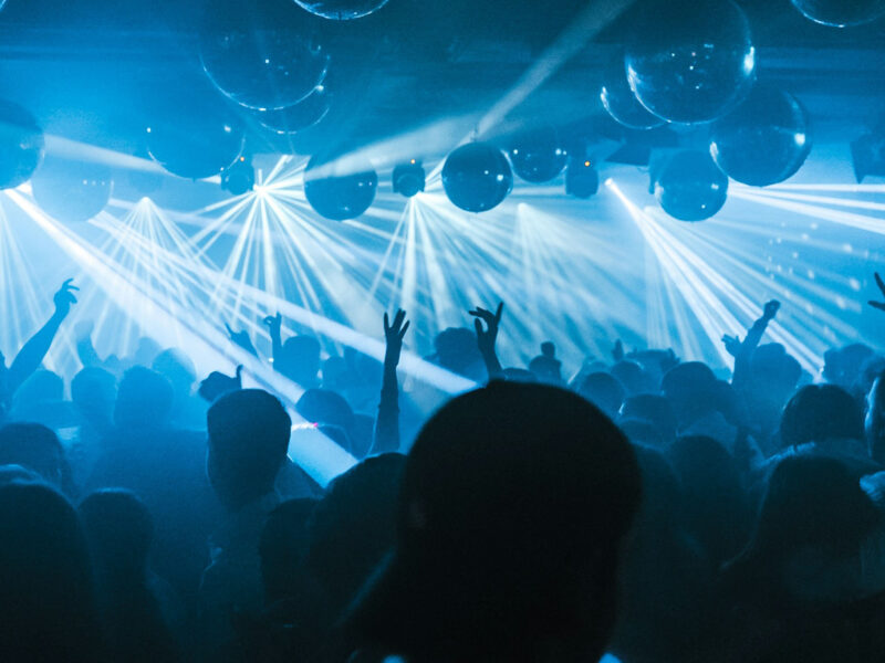 A blue lit room with balloons and lights and dancing people listening to music