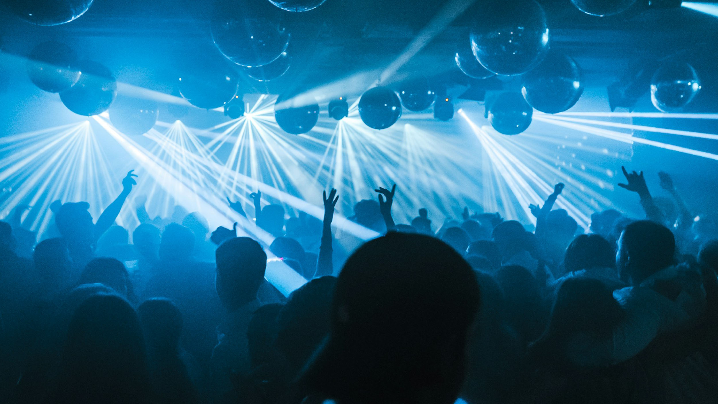 A blue lit room with balloons and lights and dancing people listening to music