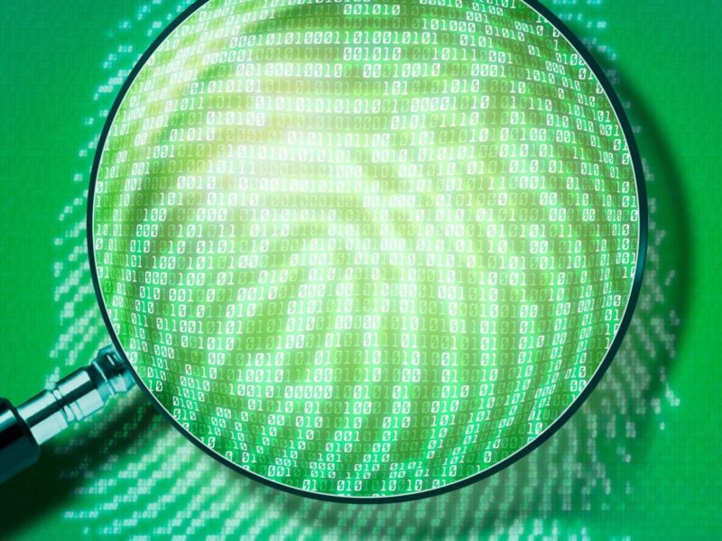 A green photo of a magnifying glass looking at a fingerprint in binary code.
