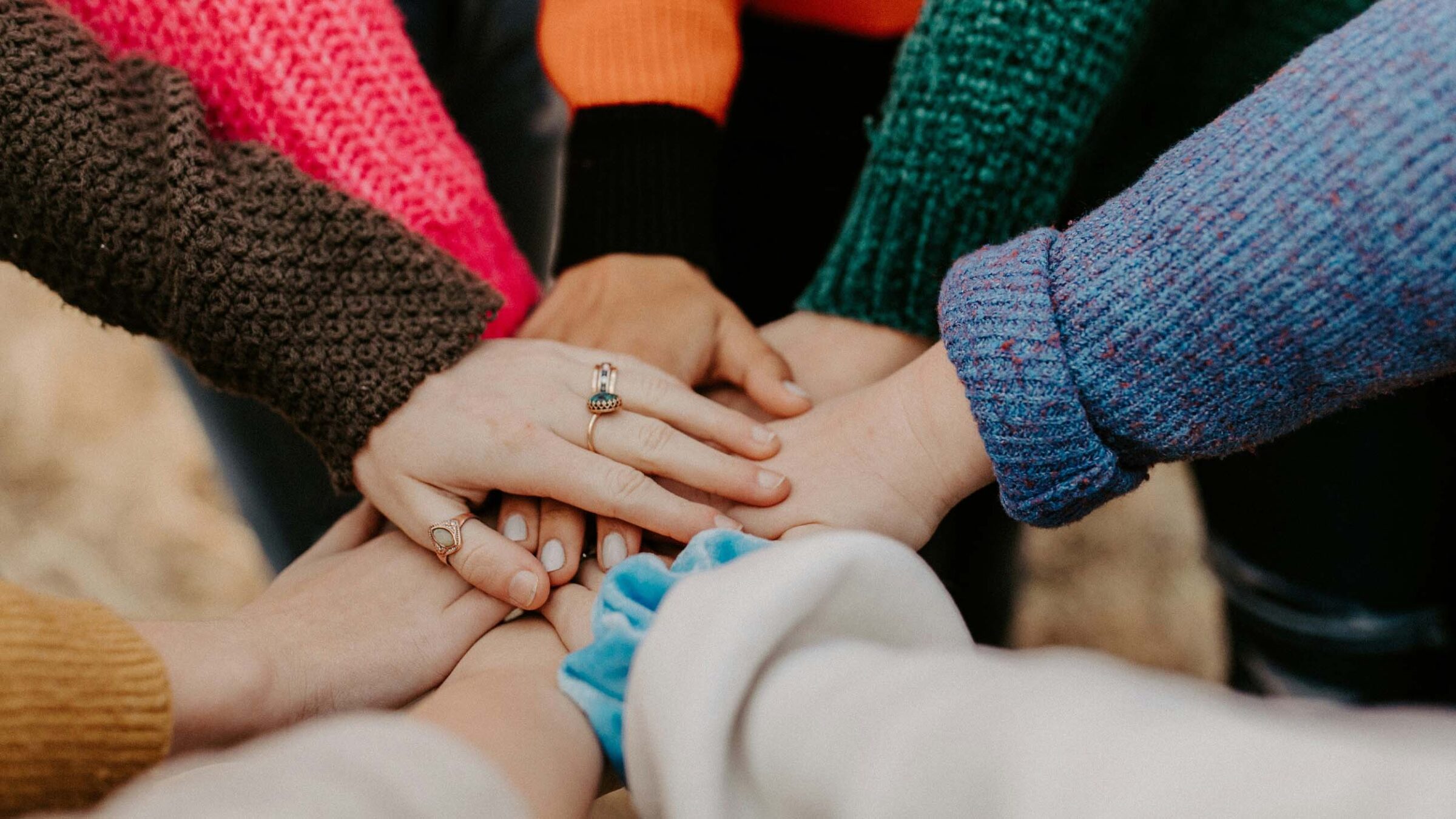 A group of people wearing colorful clothing and putting their hands together in a pile.