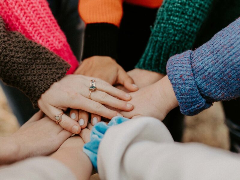 A group of people wearing colorful clothing and putting their hands together in a pile.