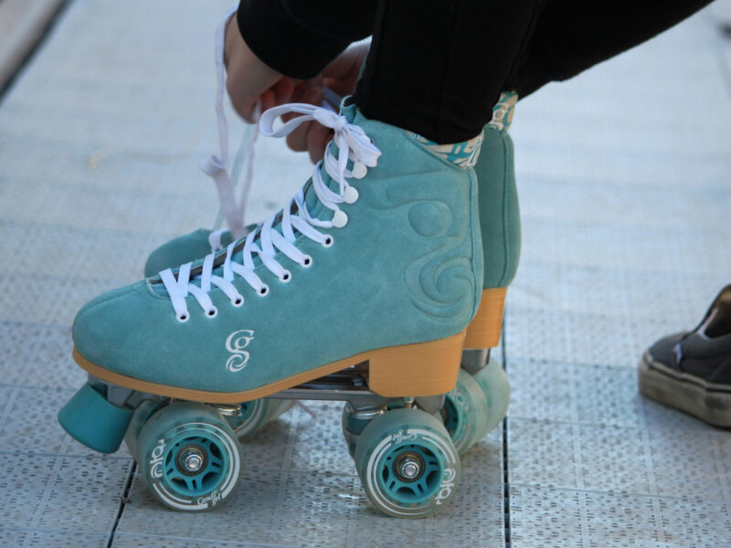 A person tying blue and orange roller skates