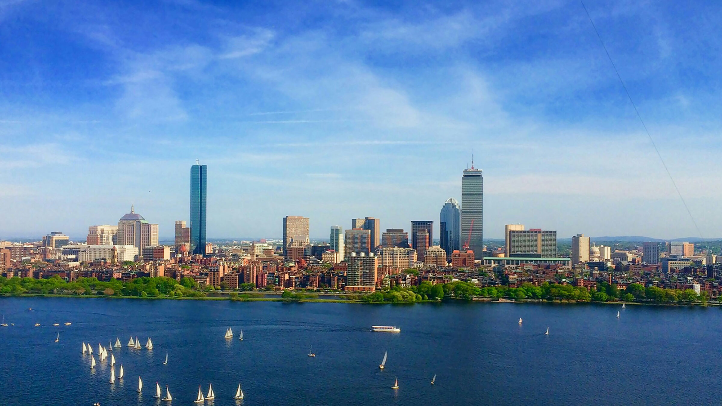 A sunny, blue sky photo of Boston with a river between the city and the camera.