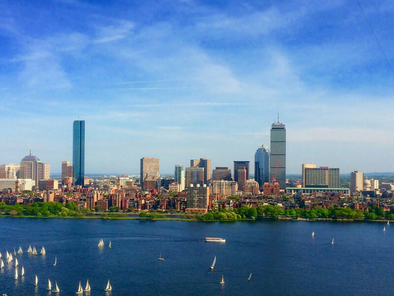 A sunny, blue sky photo of Boston with a river between the city and the camera.