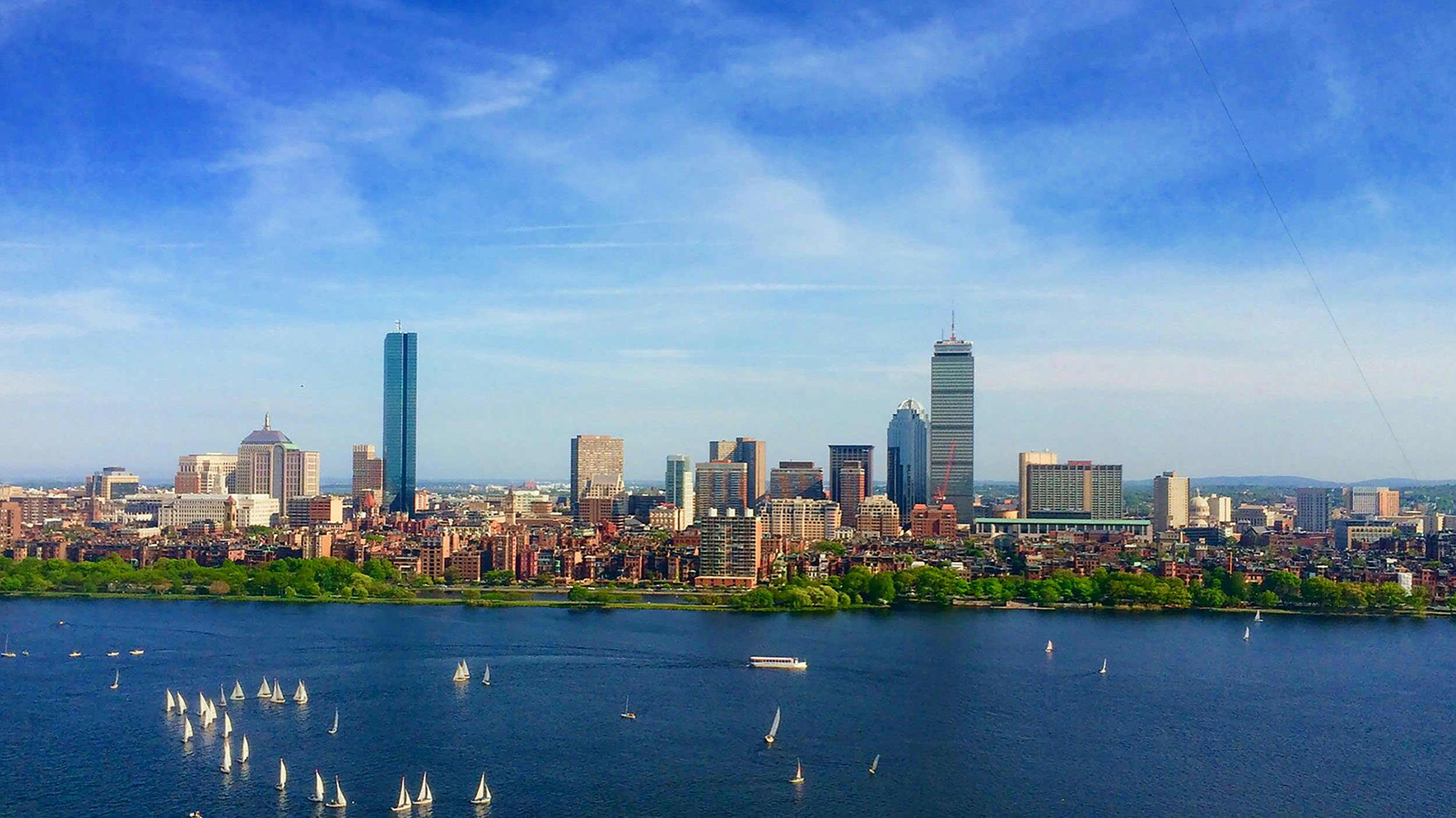 A sunny, blue sky photo of Boston with a river between the city and the camera.