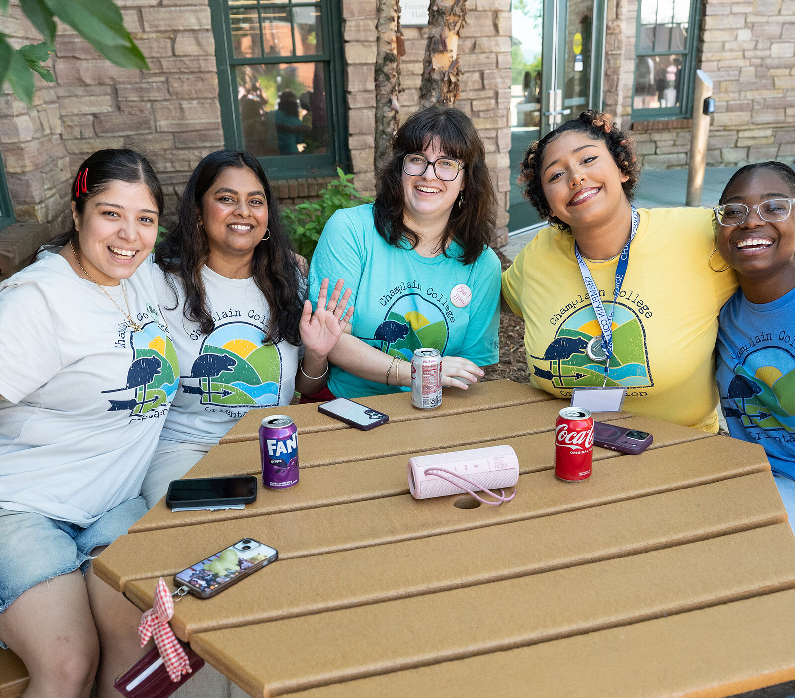 five students sit at a picnic table smiling at the camera with their hands in the air
