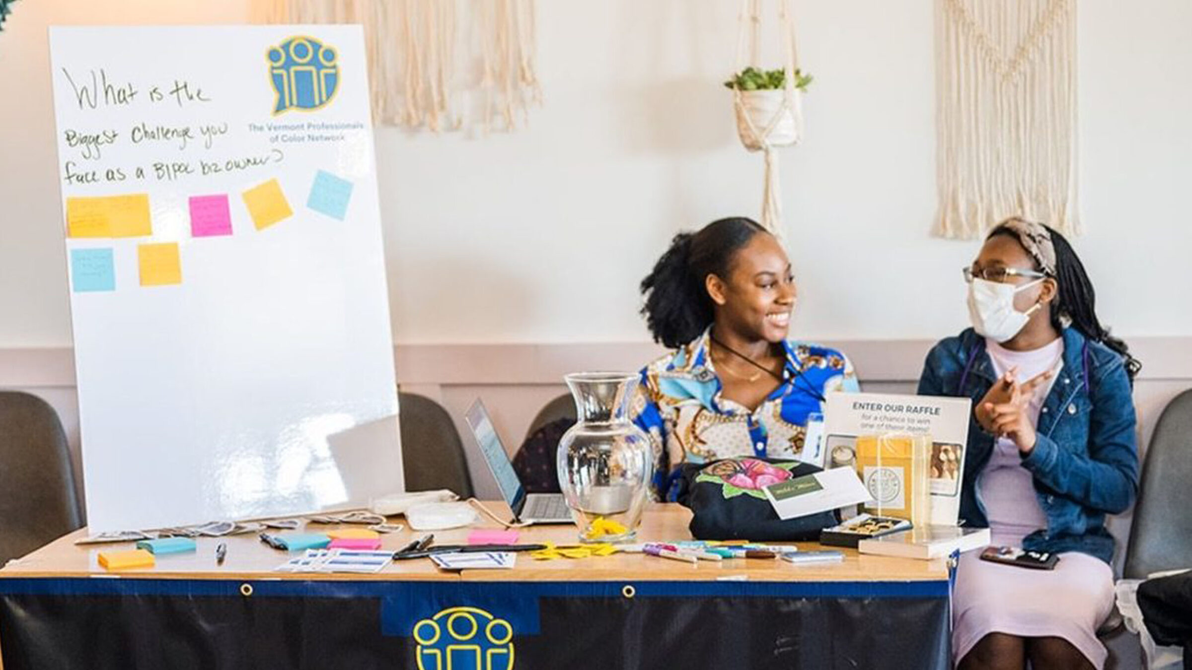 Two people sitting behind a table discussing the Vermont Professionals of Color Network with information and sticky notes.