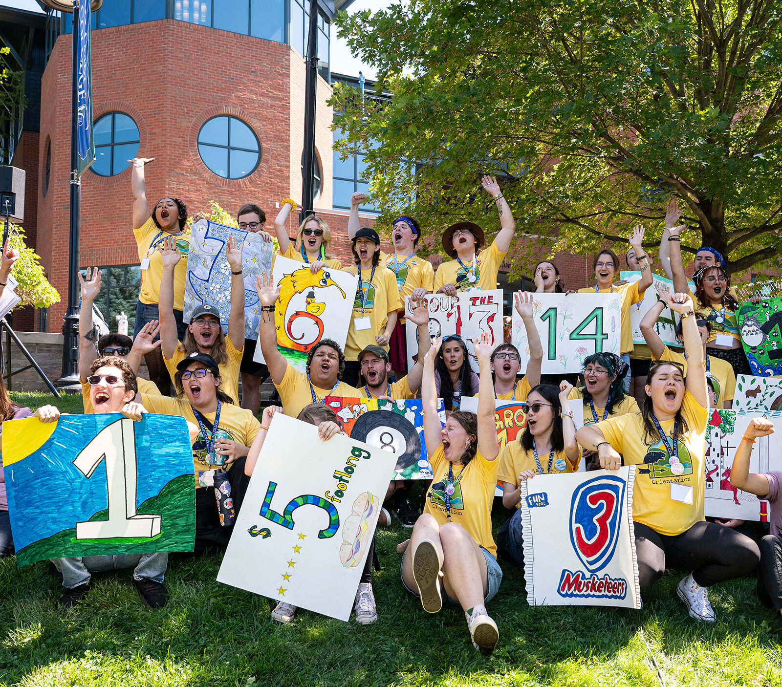 group of around 20 student orientation leaders and staff yell with excitement on the green lawn