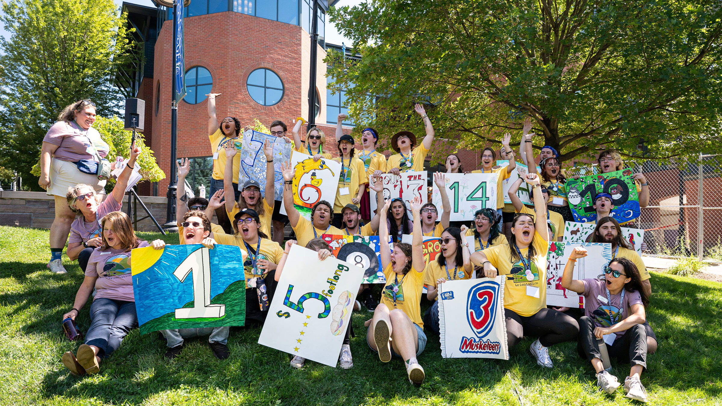 group of around 20 student orientation leaders and staff yell with excitement on the green lawn