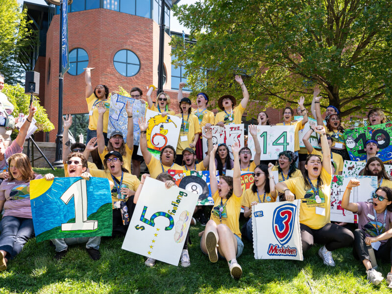group of around 20 student orientation leaders and staff yell with excitement on the green lawn