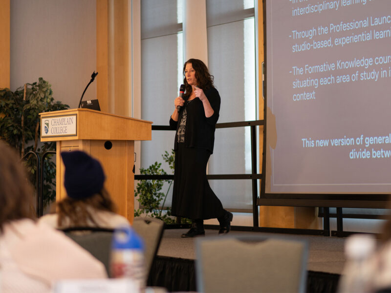 professor stands on stage with microphone in hand