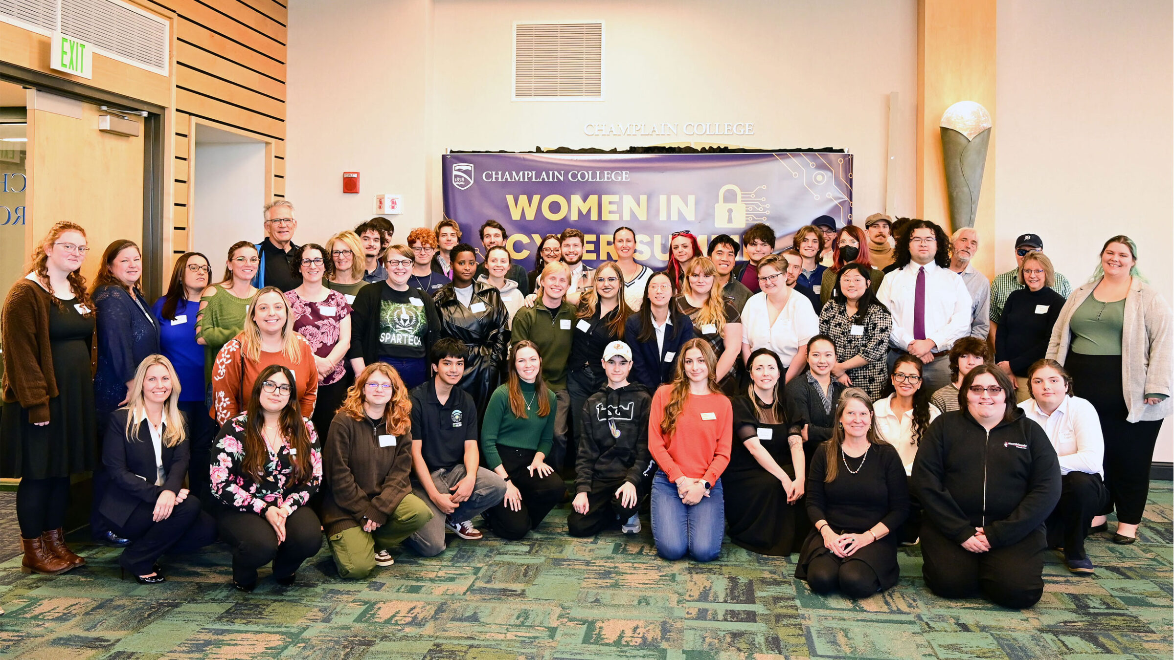 large group of women in cyber attendees pose for photo in front of a "women in cyber summit" blue sign