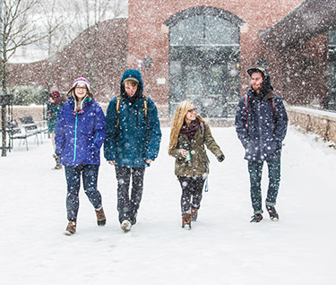 four students walking through snow on campus
