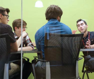 Group of students sitting around a table discussing a project in a meeting room.