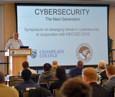 Scott Stevens, Dean of Champlain's ITS division, stands at a podium on a stage to speak about Cybersecurity