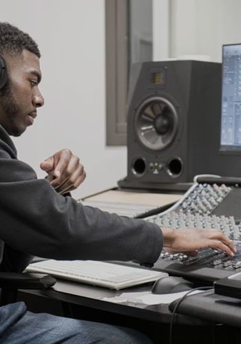 Headphones and game controller; student playing a guitar video game; student mixing audio in the sound studio.