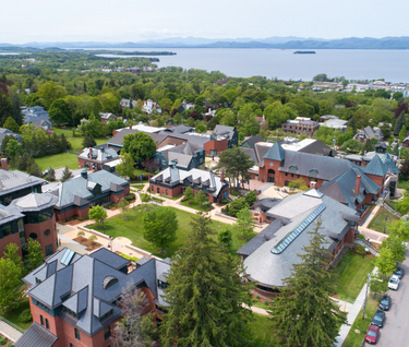springtime aerial photo of campus buildings and quads with Lake Champlain and mountains in the distance