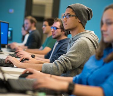 Line of students sitting at desks and working in a computer lab
