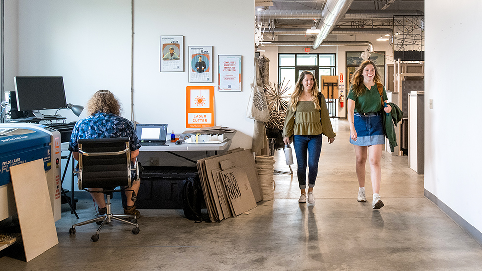 two students walk through a large open space whiel a person works at a desk