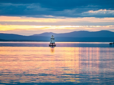 Sunset reflecting on Lake Champlain with a small light buoy set against the silhouette of the Adirondack Mountain range.
