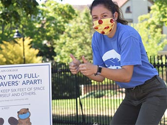 A masked student tour guide gives a thumbs up to a sign about masking on campus