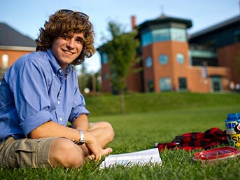 Smiling student sits, reading on the lawn on campus